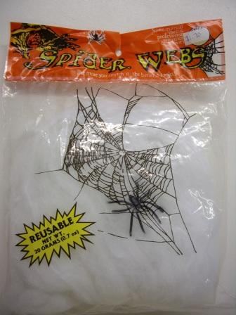 A package labeled "Giant Spider Webs White" contains decorative artificial webbing. The packaging features web graphics, a spider illustration, and includes a yellow starburst that reads "Reusable Net Wt. 20 Grams (0.7 oz).